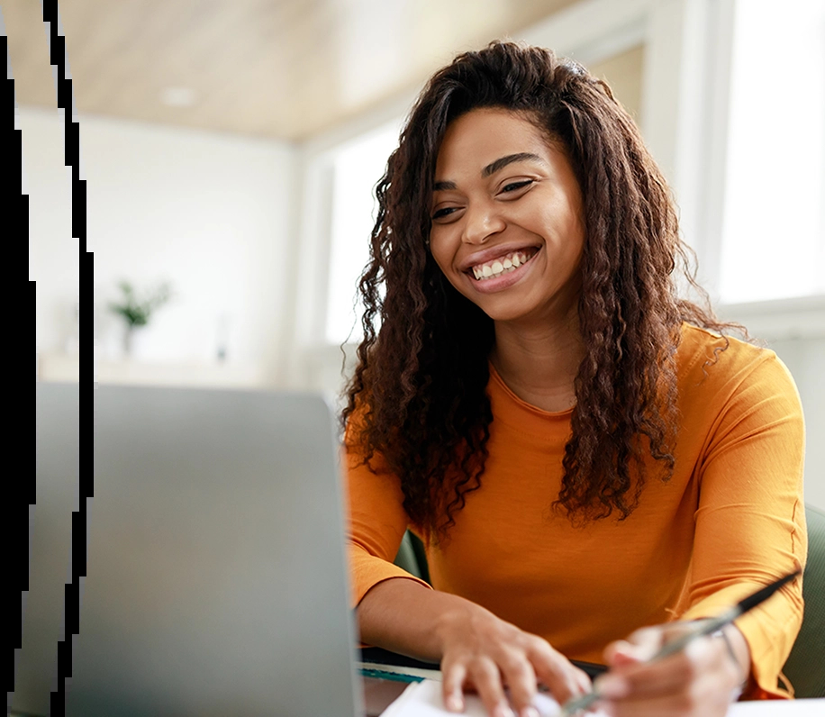 Mulher sorridente, de cabelos cacheados, usando uma blusa laranja enquanto usa um nootbook. Ela faz anotações em um caderno. Há um ícone de wi-fi no canto, parte da identidade visual da Brisanet.